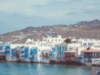 Picturesque Greek seaside town with white architecture, blue shutters, and calm waters.