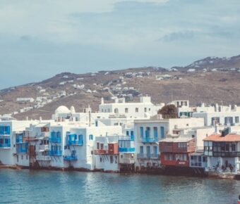 Picturesque Greek seaside town with white architecture, blue shutters, and calm waters.