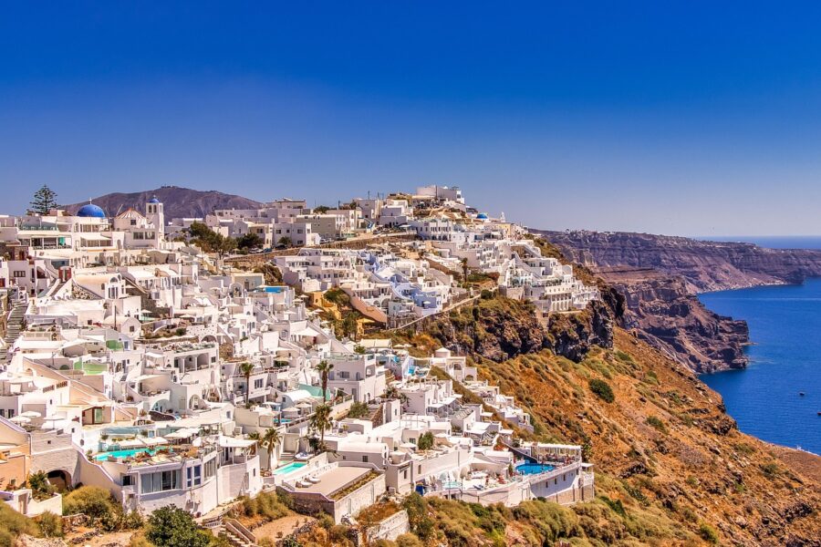 Santorini coastal village with whitewashed buildings, blue sea, and cliffs in serene Mediterranean setting.