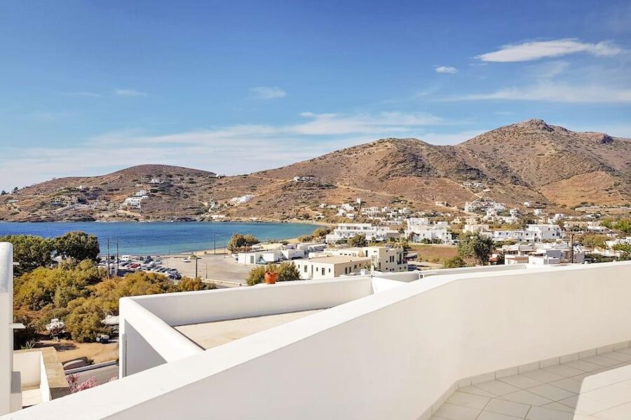 Mediterranean coastal view with terrace, beach, boats, hills, and whitewashed architecture.