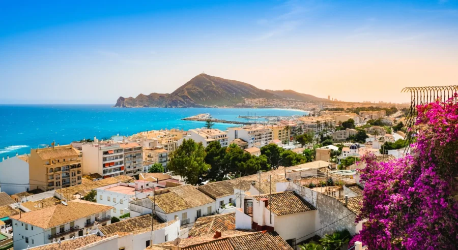 Picturesque Alicante coastal town with white buildings, terracotta roofs, vibrant sea, and lush mountains.