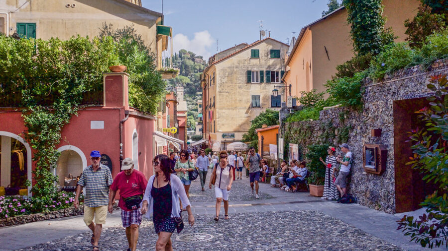 Portofino sunlit Mediterranean cobblestone street with colorful shops and strolling tourists.
