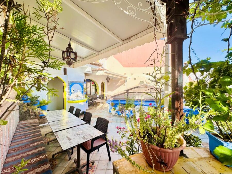 Mediterranean courtyard terrace dining area with wooden table, Moroccan lanterns, lush plants, and arches.