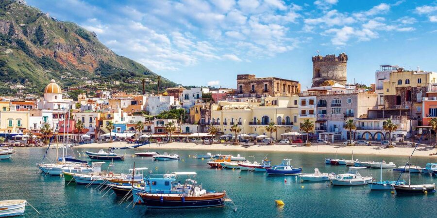 Ischia Mediterranean harbor with turquoise water, colorful boats, pastel seaside town and mountain.