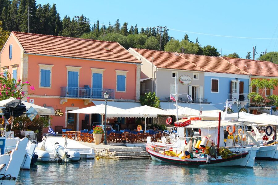 Picturesque Mediterranean harbor with boats, outdoor dining, and colorful buildings basking in sunlight.