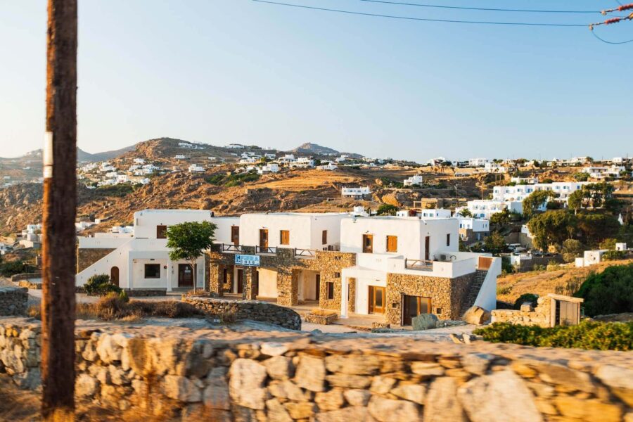 Greek hillside village with whitewashed buildings, stone structures, and terraced hills at sunset.