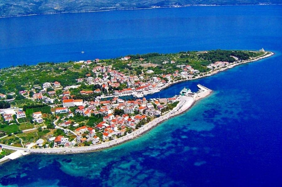 Aerial view of a serene Mediterranean island with lush greenery, vibrant houses, and a charming harbor.