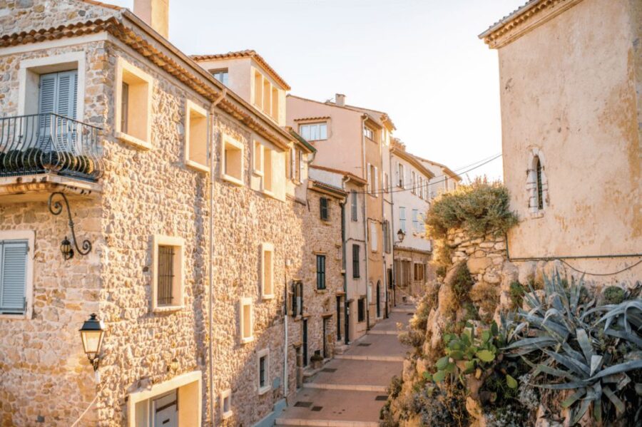 Sunlit Antibes Old Town narrow Mediterranean cobblestone street with stone buildings and balcony.
