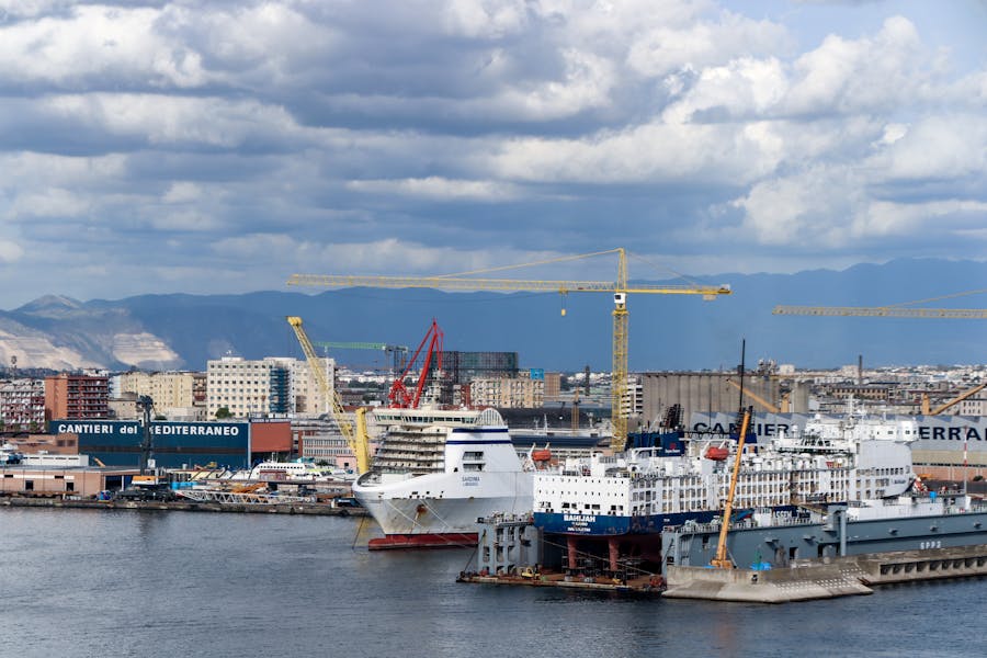 Mediterranean port shipyard with ferries, cranes, and industrial waterfront.
