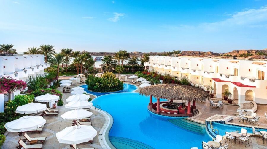 Luxury Mediterranean resort pool with swim-up bar, sun loungers, palm trees, and sea view.