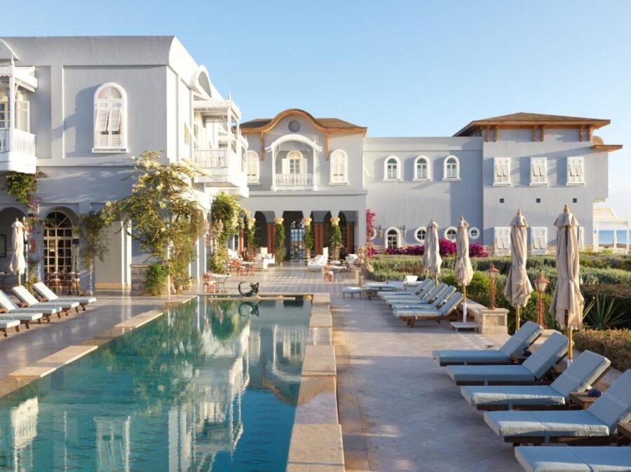 Luxury Mediterranean resort poolside terrace with turquoise swimming pool, sun loungers, and sea view.
