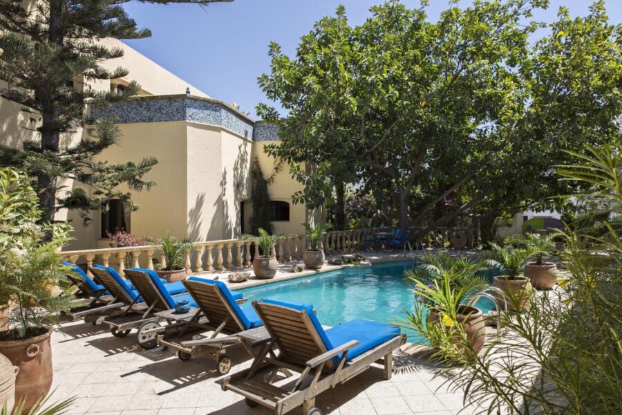 Luxury Mediterranean villa poolside with blue loungers, lush garden, and sunlit private oasis.