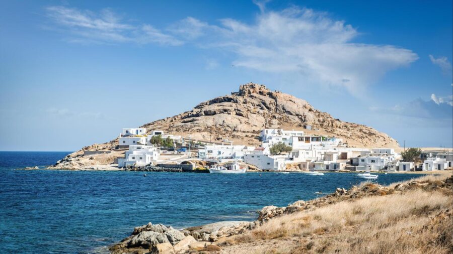 Mediterranean coastal village with rocky hill, azure waters, and whitewashed buildings.