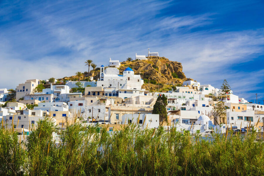 Whitewashed Mediterranean hillside village with blue dome, lush greenery, under vibrant blue sky.