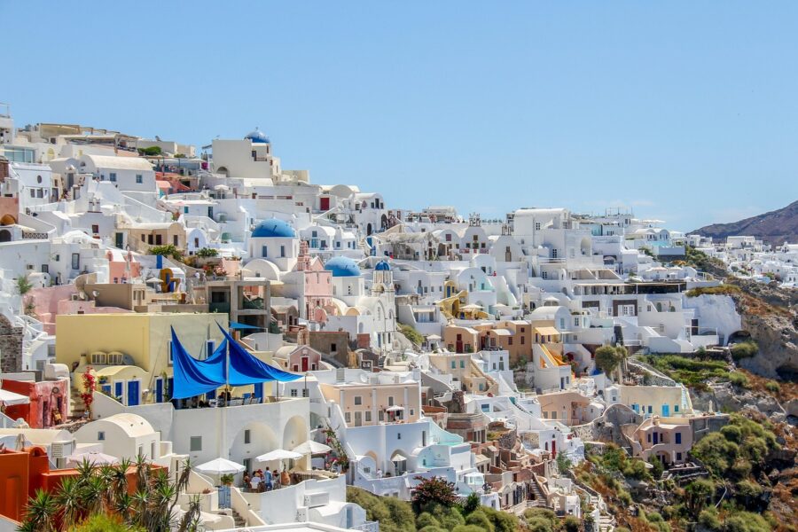 Santorini hillside village with white houses, blue domes, and lush greenery under clear skies.