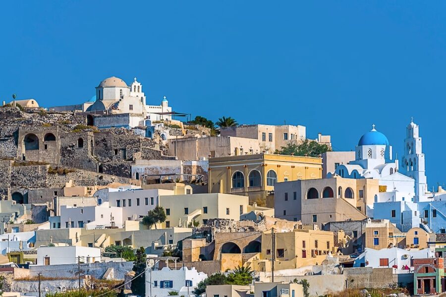 Picturesque Mediterranean hillside town with whitewashed architecture, blue dome, and lush greenery.
