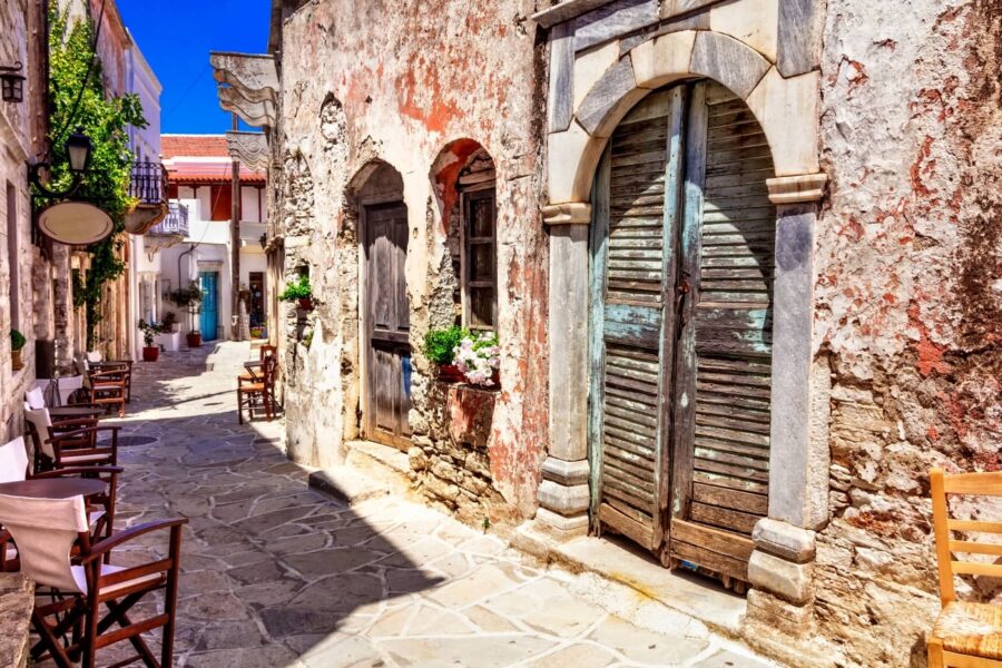 Charming sunlit Mediterranean alleyway with rustic buildings and vibrant flowers.