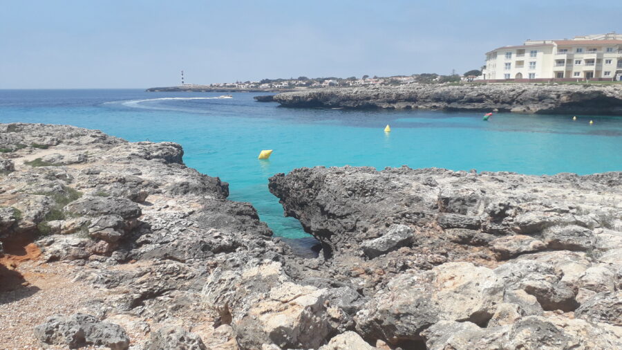 Panoramic view of a rocky shoreline on Menorca, showcasing rugged cliffs and clear blue waters.