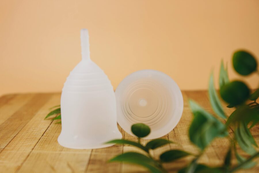 Translucent silicone menstrual cups on wooden surface with eco-friendly leaves and warm orange background.
