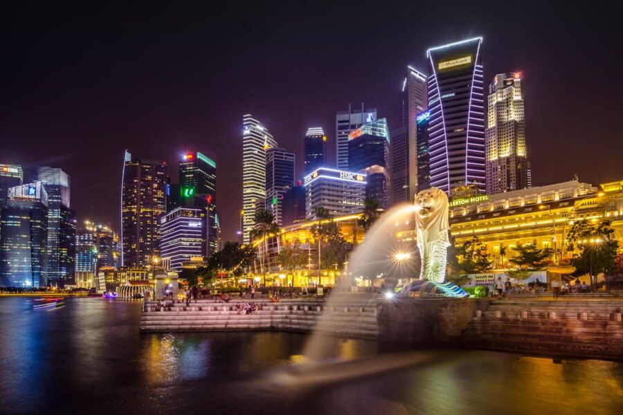 Singapore Marina Bay skyline at night with illuminated Merlion statue and calm bay waters.