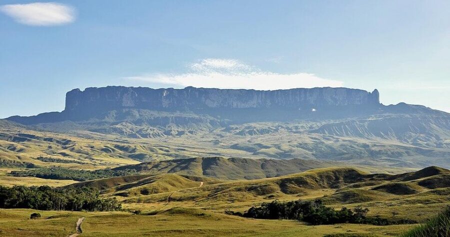 Majestic tepui mountain with flat summit, grassy plains, and a winding path under a clear sky.