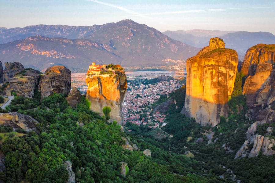 Aerial view of Meteora monastery atop sandstone rock pillars in Greece at golden hour.
