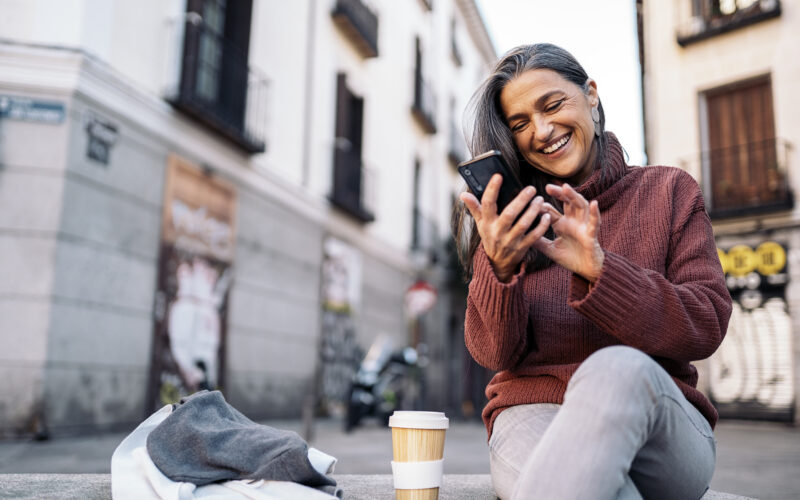 Older woman in urban setting enjoying smartphone, reflecting modern, independent lifestyle.