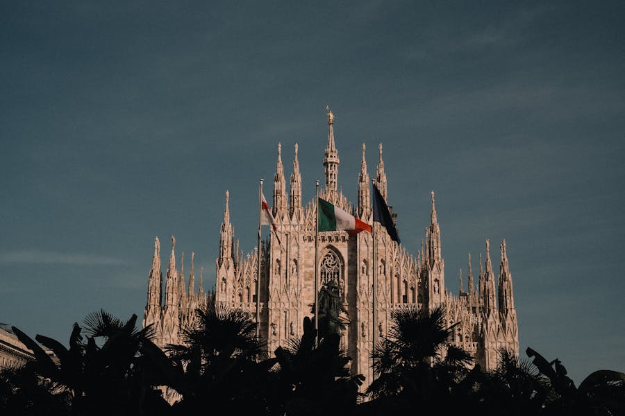 Milan Cathedral at twilight, Gothic architecture, Italian flags, palm trees, historic and majestic.