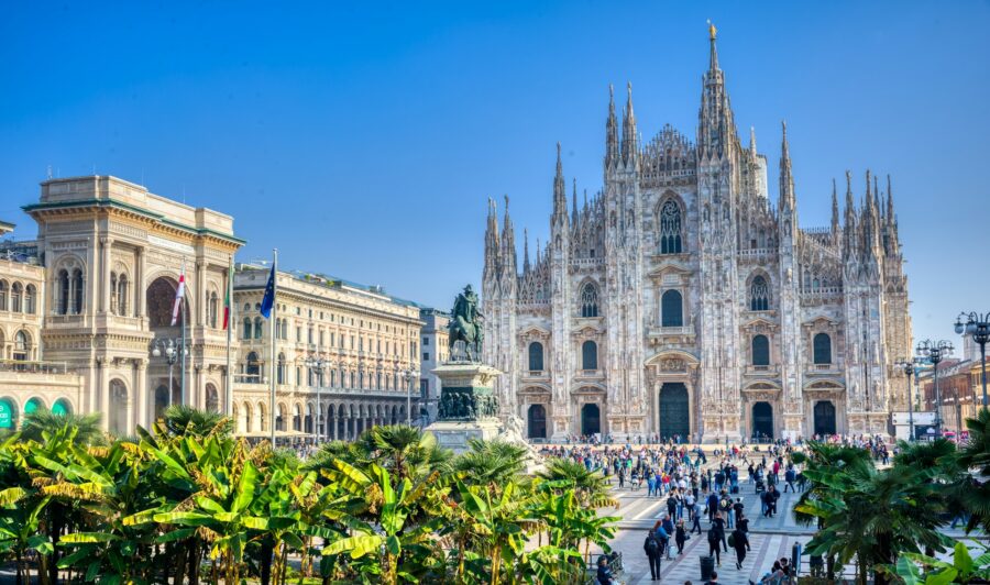 Milan Duomo cathedral and Piazza with tourists, ornate Gothic facade and equestrian statue.