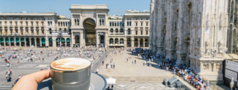Cappuccino sits on a table in Galleria Vittorio Emanuele II, with elegant architecture and bustling shoppers in the background.