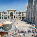 Cappuccino sits on a table in Galleria Vittorio Emanuele II, with elegant architecture and bustling shoppers in the background.