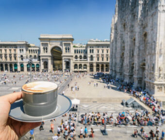 Cappuccino sits on a table in Galleria Vittorio Emanuele II, with elegant architecture and bustling shoppers in the background.
