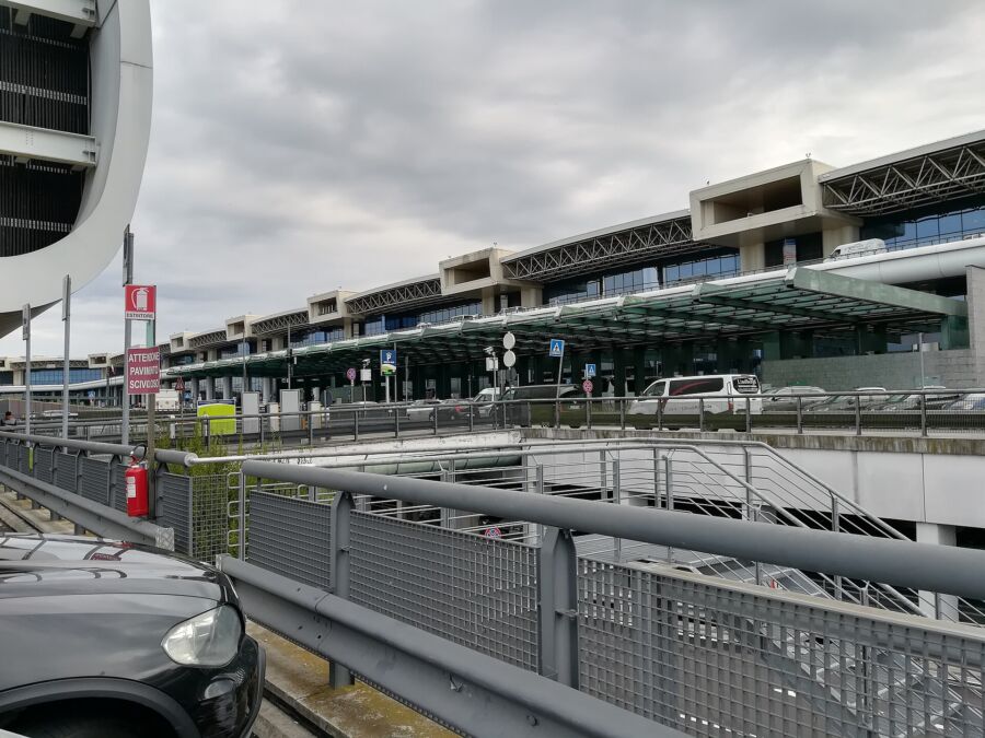 Car parked in front of the Milan Malpensa Airport terminal, showcasing the modern architecture of the building.
