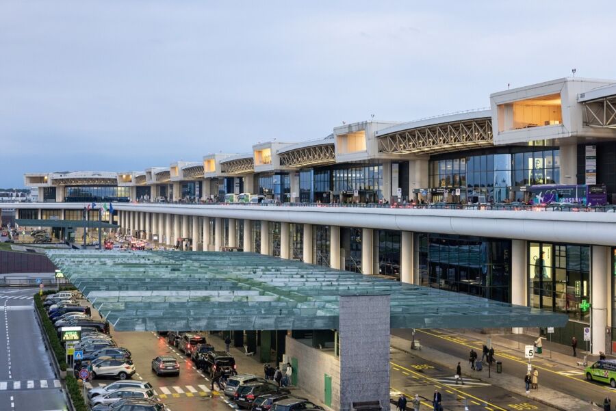 Milan Malpensa Airport terminal depicted, featuring a spacious interior filled with travelers and shops