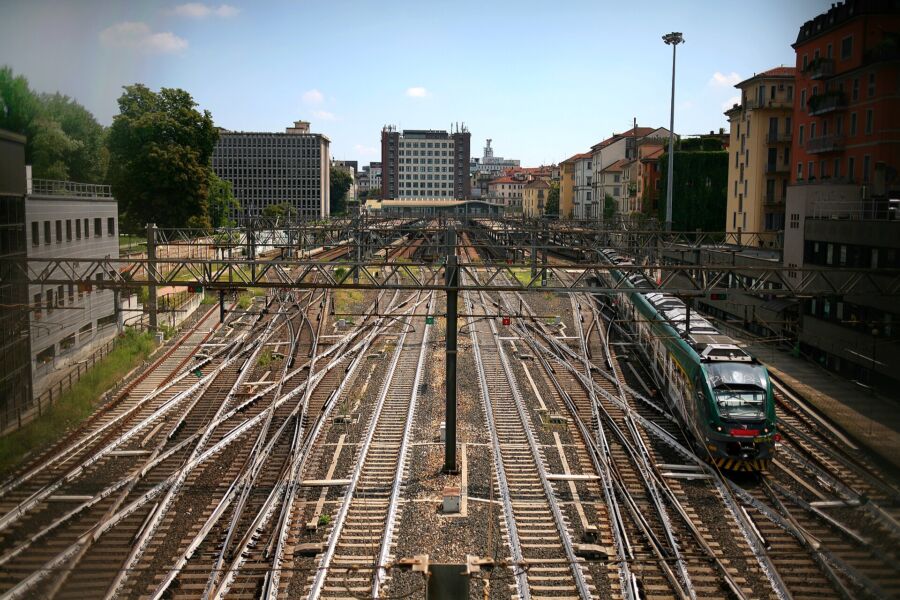 Train on the tracks, identified as the Milan Malpensa service, moving through a scenic landscape.
