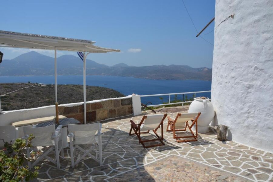 Chairs and an umbrella on a patio provide a stunning sea view at Milos Vaos Windmill accommodation in Greece.