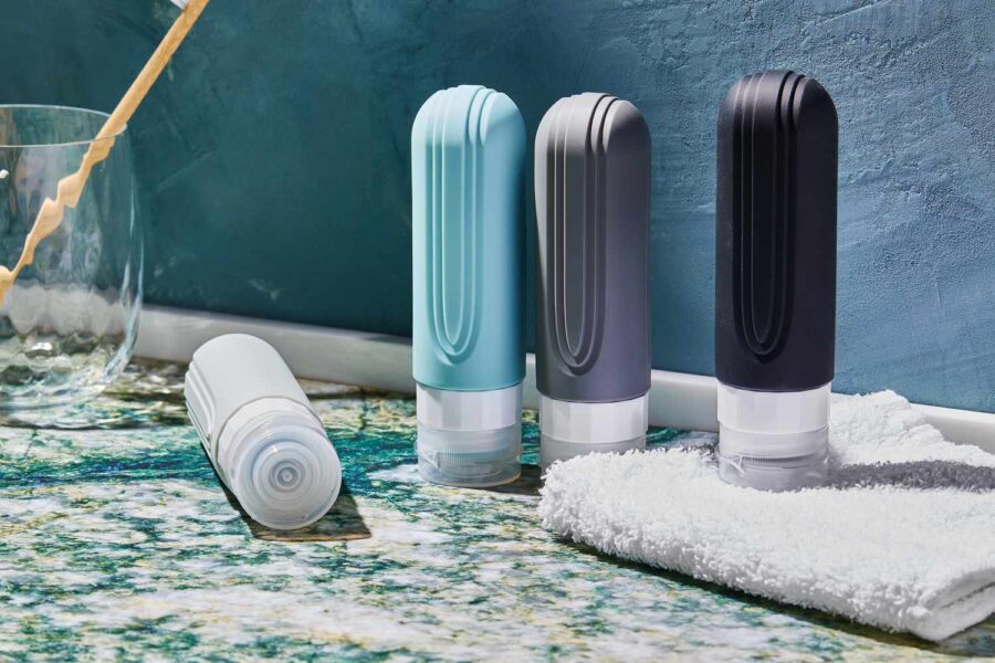 Minimalist refillable travel toiletry bottles on marble bathroom counter with towel and glass.