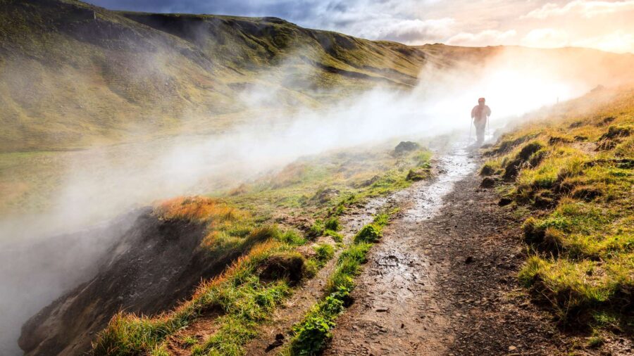 Misty landscape with figure walking on path through lush hills at sunrise.