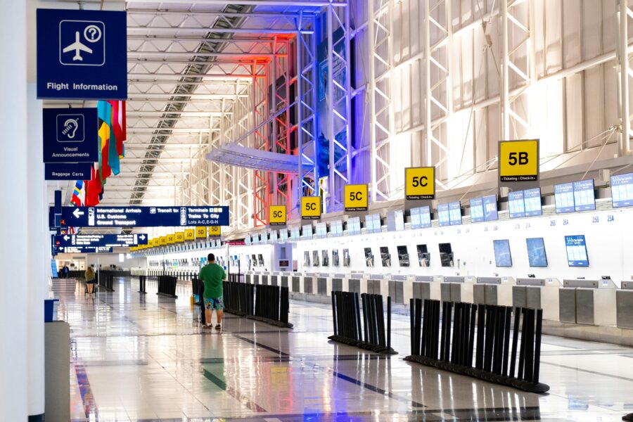 Modern airport terminal with traveler, self-check-in kiosks, natural lighting, and international flags.