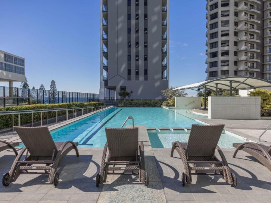 Luxury Broadbeach apartment infinity pool with wicker loungers, high-rise oceanfront skyline, sunny resort.