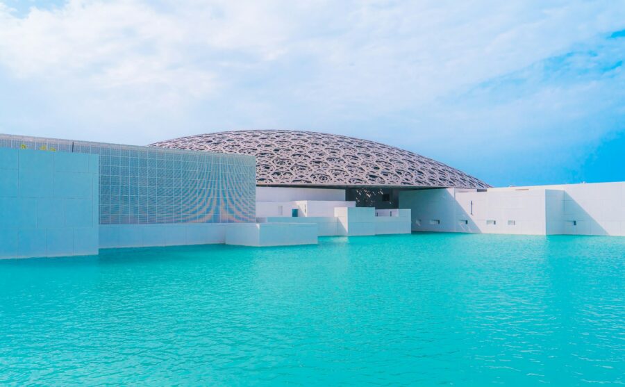 Louvre Abu Dhabis dome: modern architecture, light play, turquoise water, geometric design, serene atmosphere.