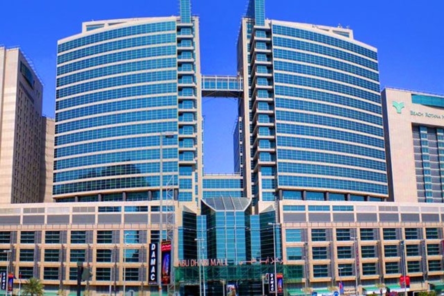 Abu Dhabi Mall complex with futuristic glass architecture and palm trees against clear blue sky.