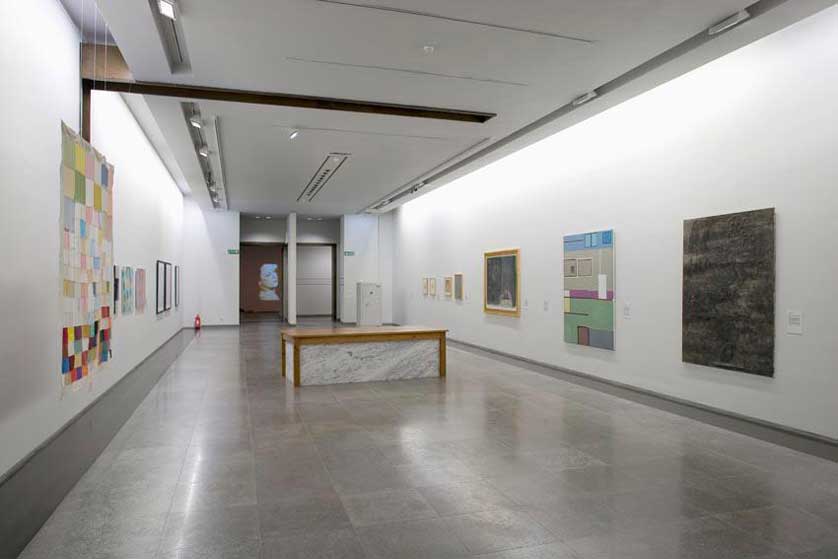 Modern art gallery interior at MNAC with white walls, artworks, bench, and lit projection.