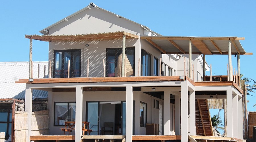 Modern elevated beachfront guest house with wooden deck, oceanview terraces, and palm trees.