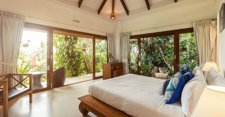 Modern bedroom with nature view, featuring glass doors, wooden elements, and tranquil ambiance.