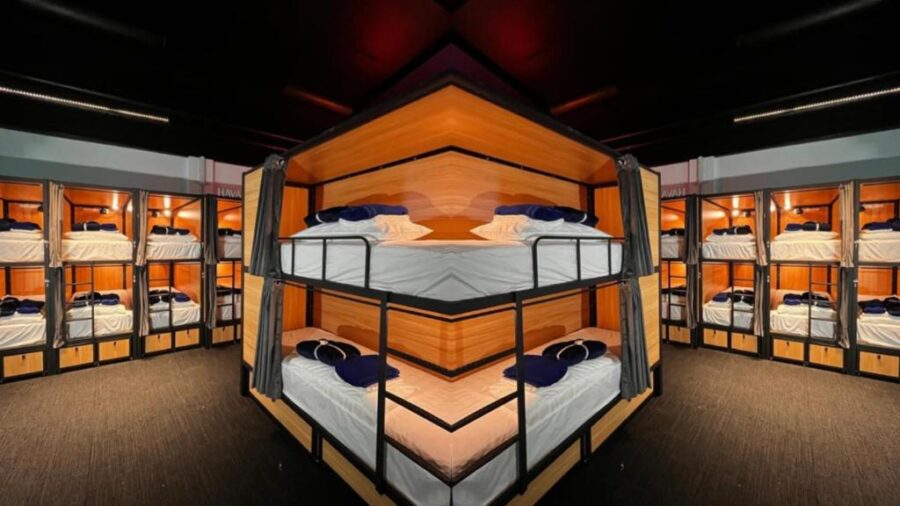 Modern capsule hostel dorm with stacked bunk beds, private sleeping pods, wood accents and curtains.