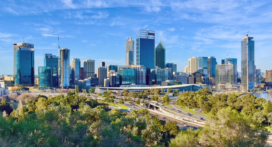 Perth CBD skyline with modern skyscrapers, riverfront, highway, and green park under blue sky.