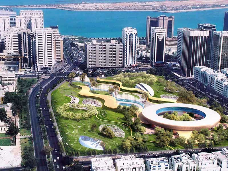Aerial view of futuristic waterfront city park with organic architecture, green lawns, and high‑rise buildings.