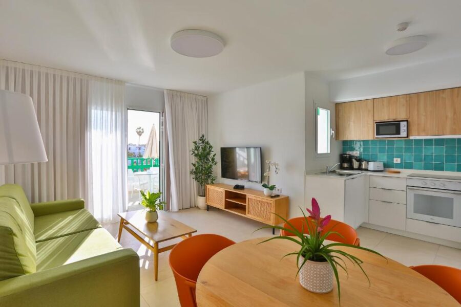 Bright modern coastal apartment living room and kitchen with balcony, green sofa, and colorful dining area.