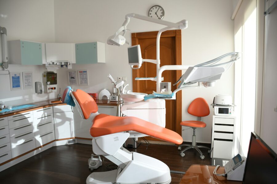 Modern dental office with orange chair, white cabinets, and advanced dental equipment.